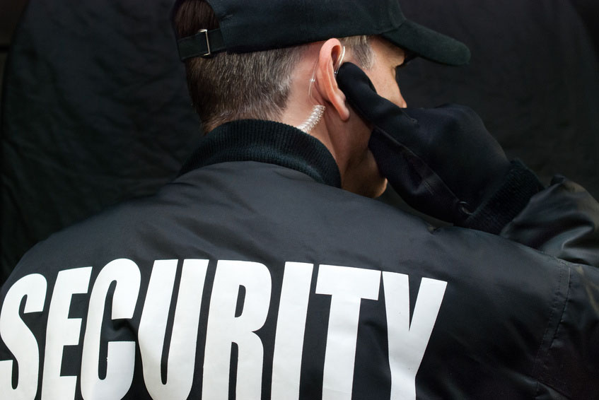 Close-up of a security guard listening to his earpiece. Back of jacket showing.